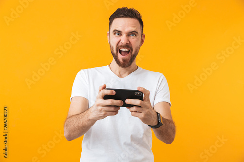Hhappy man posing isolated over yellow wall background play games by phone. © Drobot Dean