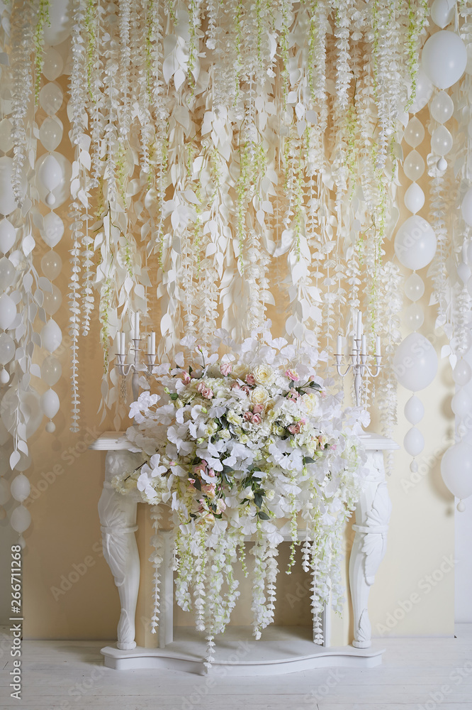Flower garland on the wall as an element of festive, wedding decor. Light tone. Decorative fireplace.