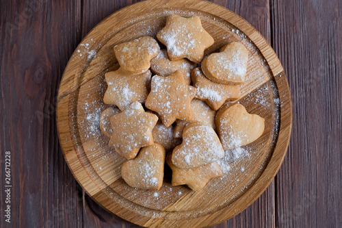 Homemade cookies with powdered sugar on a board on a brown wooden background, top view