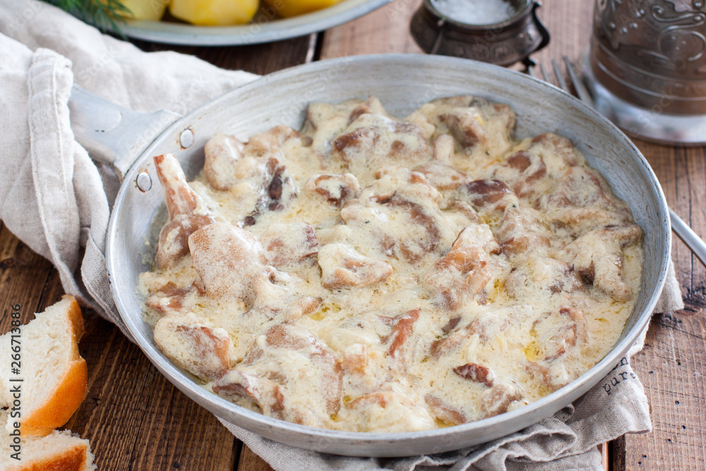 Forest mushrooms in sour cream sauce on a pan on a wooden table, horizontal Forest mushrooms in sour cream sauce on a pan on a wooden table, horizontal