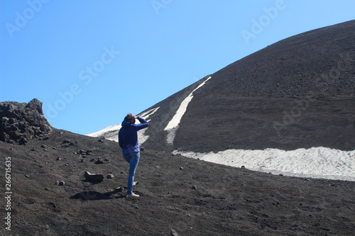 Young woman visiting Etna Park in Sicily with its black lava ash and snow fields