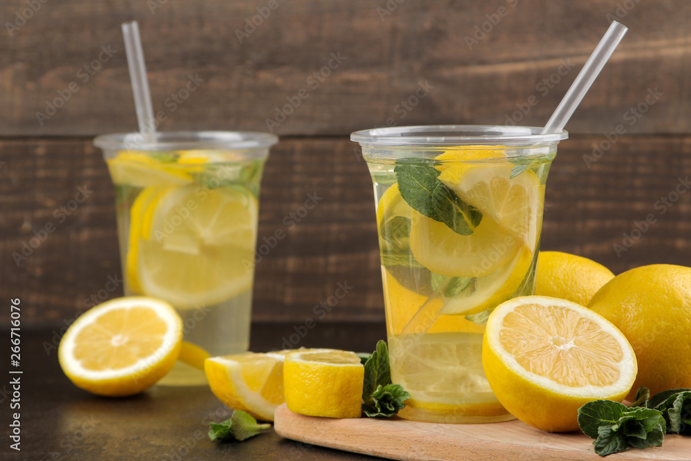 Homemade lemonade with mint and lemon in plastic glasses on a brown background. Refreshing lemonade drink. Homemade lemonade with mint and lemon in plastic glasses on a brown background. Refreshing lemonade drink.