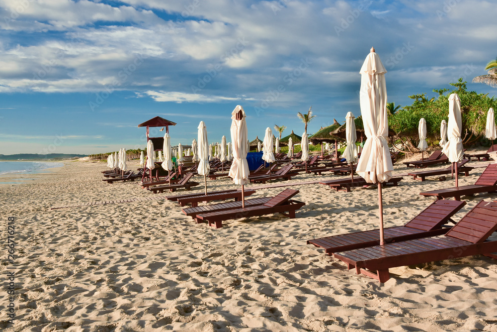 Sun loungers and umbrellas on an empty sandy beach. Summer sunny cloudy blue sky. Kamran. Vietnam.