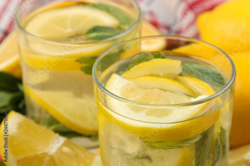 Homemade lemonade with mint and lemon in plastic glasses on a natural wooden background. Refreshing lemonade drink. close-up