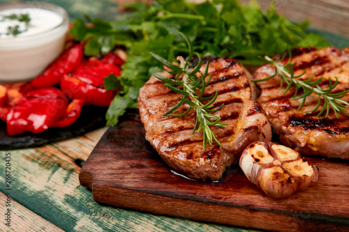 Steak pork grill on wooden cutting board with a variety of grilled vegetables.