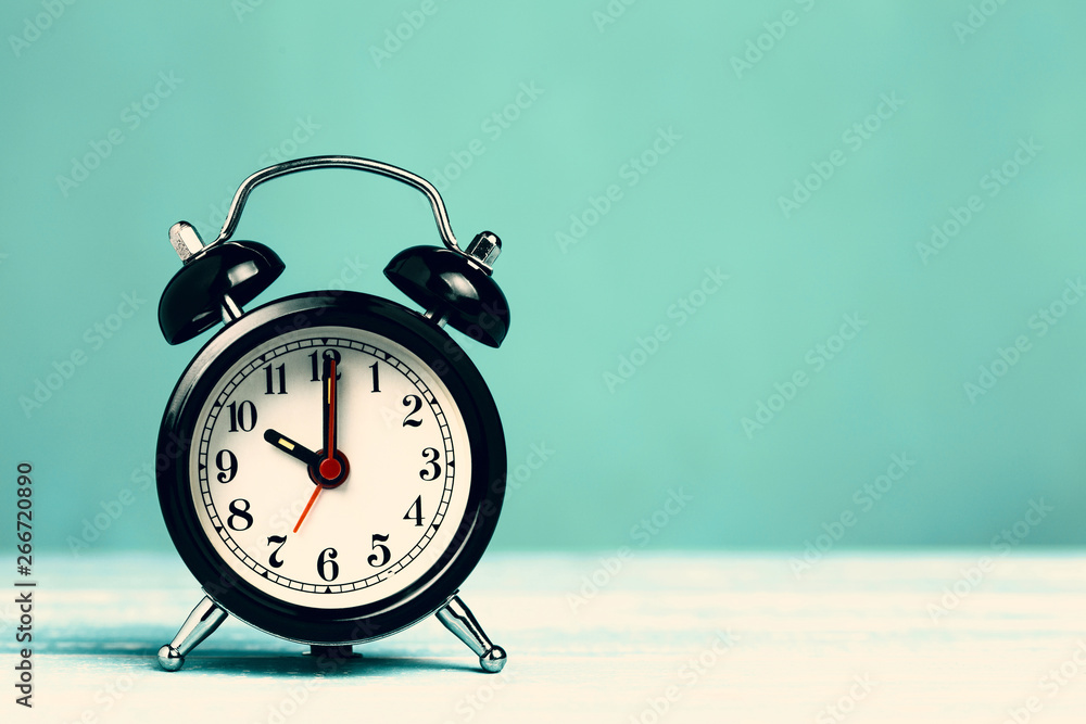 Retro black alarm clock on turquoise background with copy space. Alarm