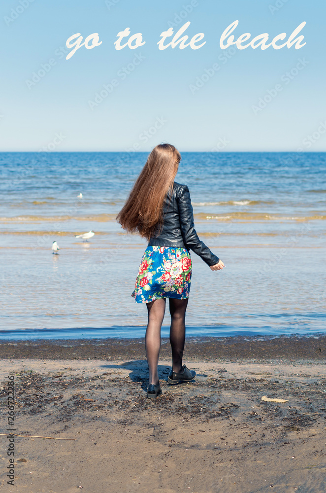 'Go to the beach' text. Anonymous girl with beautiful long chestnut hair on a beach. Sunny and windy day in Jurmola (Latvia). 