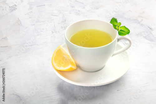 An angle view of a cup of tea with a slice of lemon and mint leaves, with a place for text