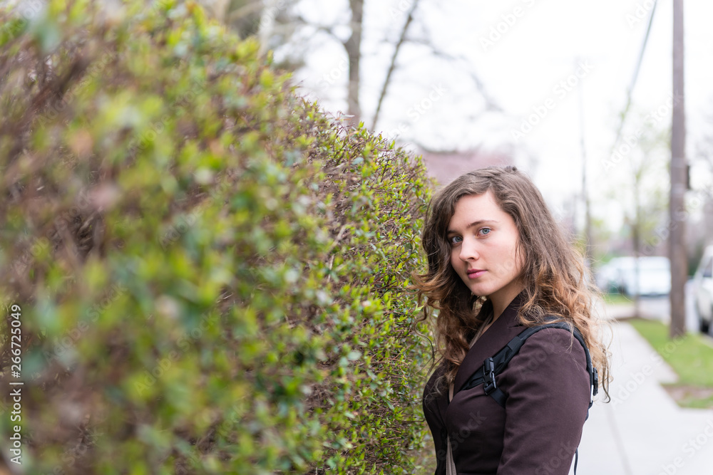 Young woman closeup portrait on sidewalk street in Washington DC, USA United States during spring with hedge green bush in University Heights residential area Young woman closeup portrait on sidewalk street in Washington DC, USA United States during spring with hedge green bush in University Heights residential area