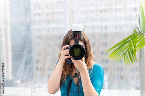 One young wedding photographer woman in dress standing with camera external flash taking picture photo and lens covering face photo