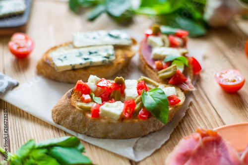 Traditional Italian bruschetta with blue cheese, feta, tomatoes, basil leaves, jamon on a wooden background.