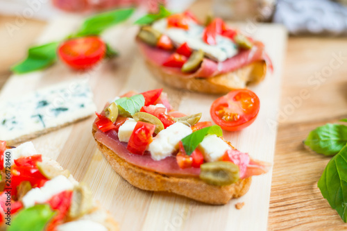 Traditional Italian bruschetta with blue cheese, feta, tomatoes, basil leaves, jamon on a wooden background.