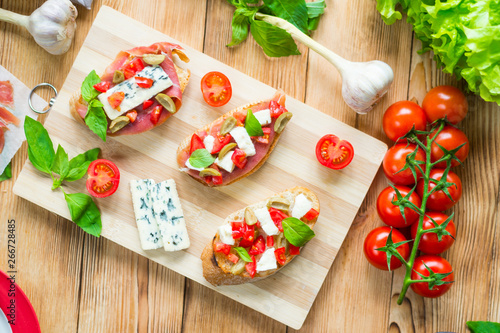Toasted ciabatta, a cheese sandwich with mold, tomatoes, basil on a wooden background.