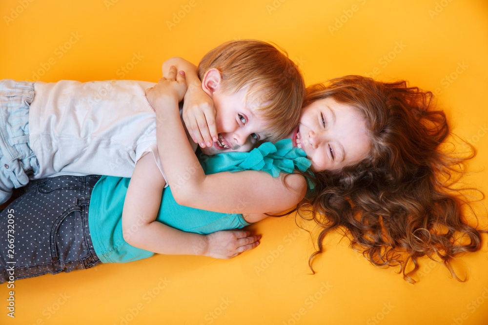 happy little brother and sister lying on a colored yellow background