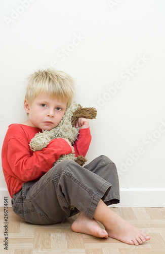 Lonely upset child sitting on the floor with his teddy bear.