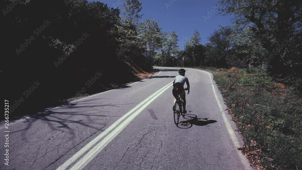 Cyclist going uphill on a beautiful paved mountain road in Greece Cyclist going uphill on a beautiful paved mountain road in Greece