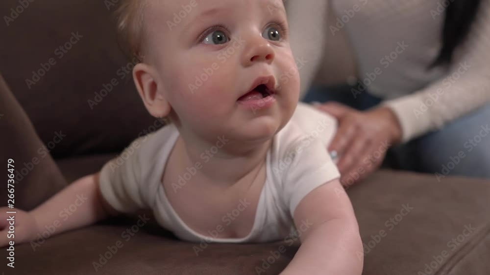 A close-up of an adorable happy caucasian infant baby lying on tummy and looking at camera with curiosity. True emotions.