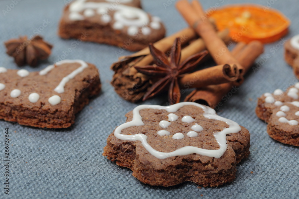 Gingerbread cookies decorated with a pattern of white glaze. On a background of gray fabric. Decorated with decorative elements of dried fruit, cinnamon sticks and anise stars.