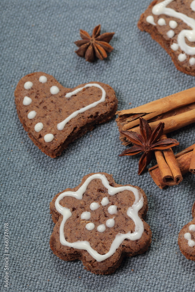Gingerbread cookies decorated with a pattern of white glaze. On a background of gray fabric. Decorated with decorative elements of cinnamon sticks and anise stars. Gingerbread cookies decorated with a pattern of white glaze. On a background of gray fabric. Decorated with decorative elements of cinnamon sticks and anise stars.