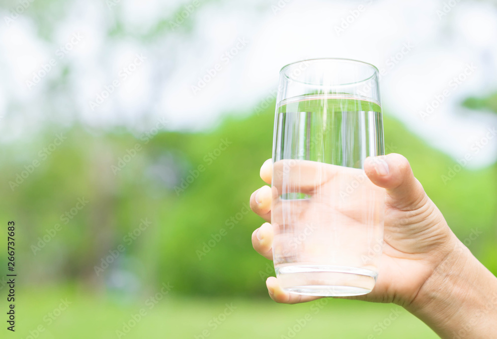 Hand holding glass of pure water on green nature background, healthy concept Hand holding glass of pure water on green nature background, healthy concept