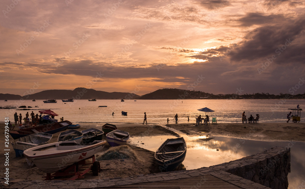 High contrast boats and tourists and locals at a bay surrounded by warm sea water at golden hour, at a beautiful summer sunset at Buzios, Brazil, next to Geriba beach