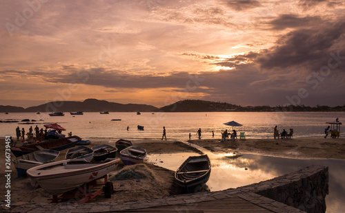 High contrast boats and tourists and locals at a bay surrounded by warm sea water at golden hour, at a beautiful summer sunset at Buzios, Brazil, next to Geriba beach photo