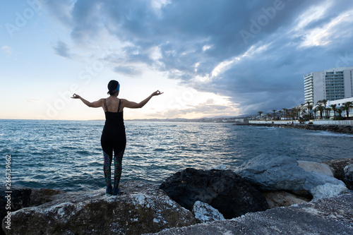 Woman practicing yoga facing the sea on a cloudy day