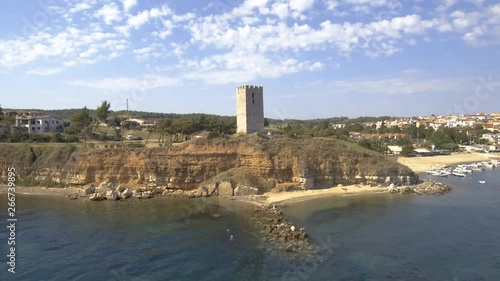 Aerial view of a medieval tower on the beach of Nea Fokea and a small boat in the harbor,Halkidiki Greece, backward movement by drone photo