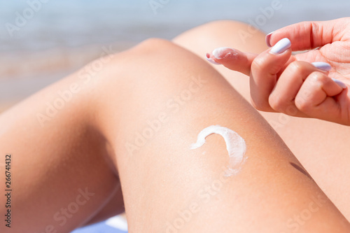 Closeup on female hand applying sunblock on her tanned leg at the beach