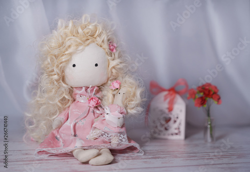Handmade doll on a white wooden table with paper flowers and gift box