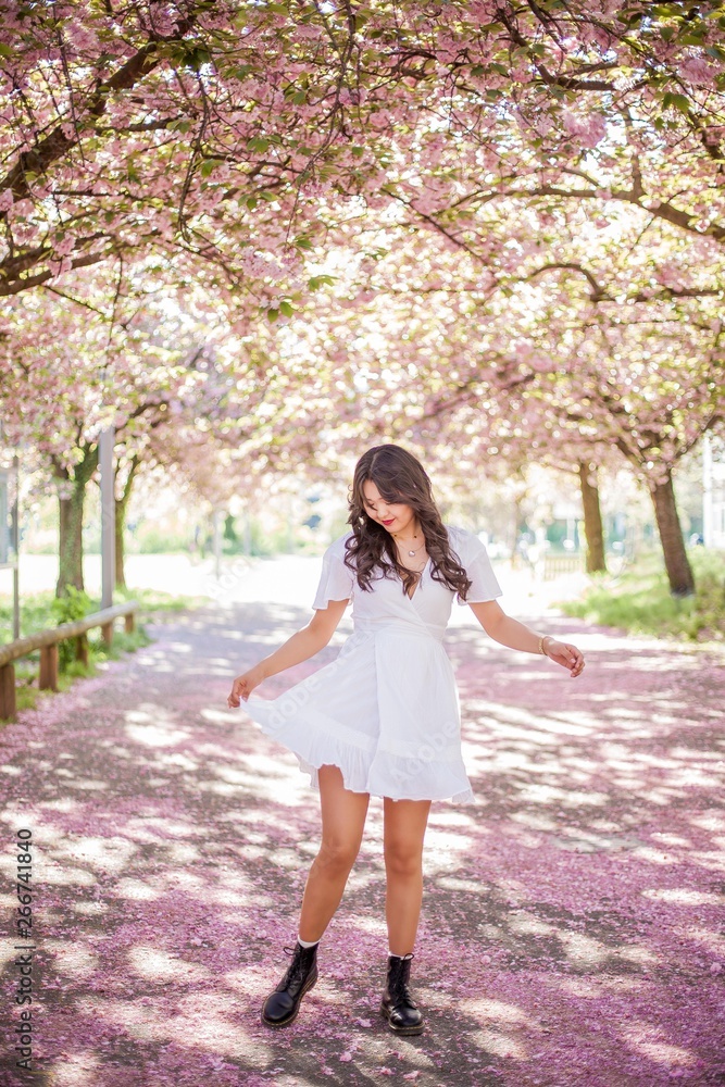 A young beautiful Asian woman in a white dress walks in a flowered park. Sakura. Blooming trees. A young beautiful Asian woman in a white dress walks in a flowered park. Sakura. Blooming trees.
