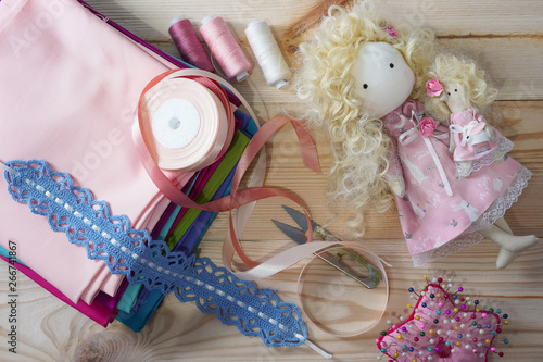 Cute handmade doll on a wooden table with colorful fabrics, knitted lace, pastel ribbons and sewing furniture photo