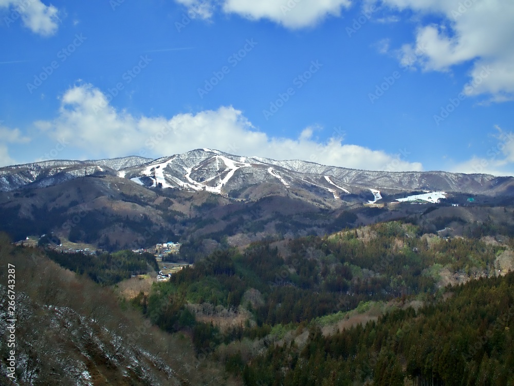 Landscape shot on the snow mountain at the far end with green background at the front with blue sky with cloud during Spring season of Japn