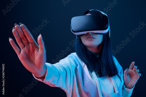 selective focus of girl gesturing while using virtual reality headset on blue