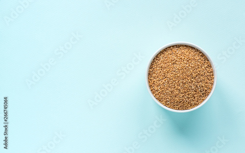 Uncooked crushed spelt in a white bowl on pastel blue background. Top view, copy space, minimal idea