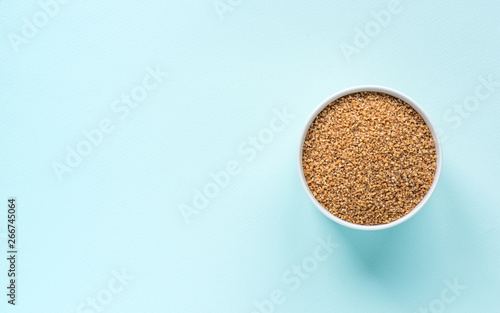 Photography Uncooked crushed spelt in a white bowl on pastel blue background