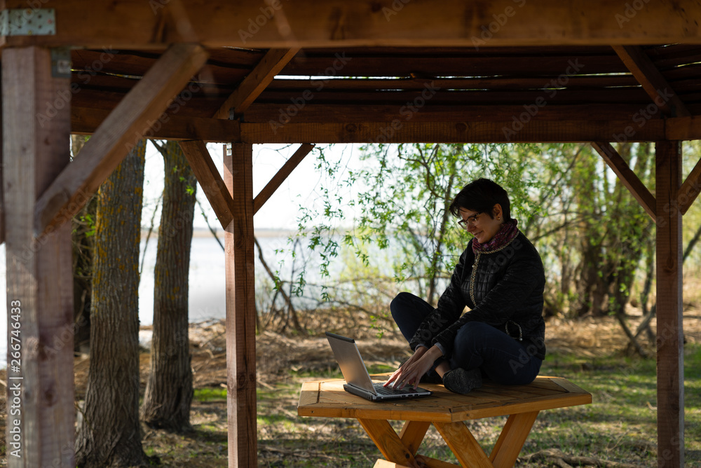 Girl using lap top among nature. Time online. The girl is sitting at the computer on the table in the summer house. Girl using lap top among nature. Time online. The girl is sitting at the computer on the table in the summer house.