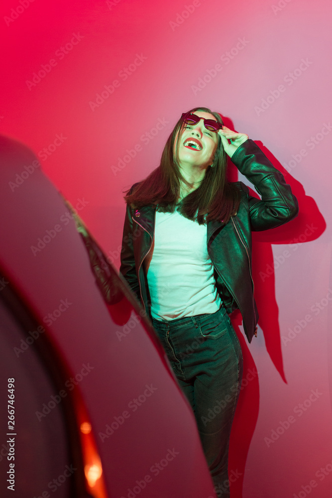 Fashioned girl in leather jacket in dark glasses in pink and blue neon lights background. Fashioned girl in leather jacket in dark glasses in pink and blue neon lights background.