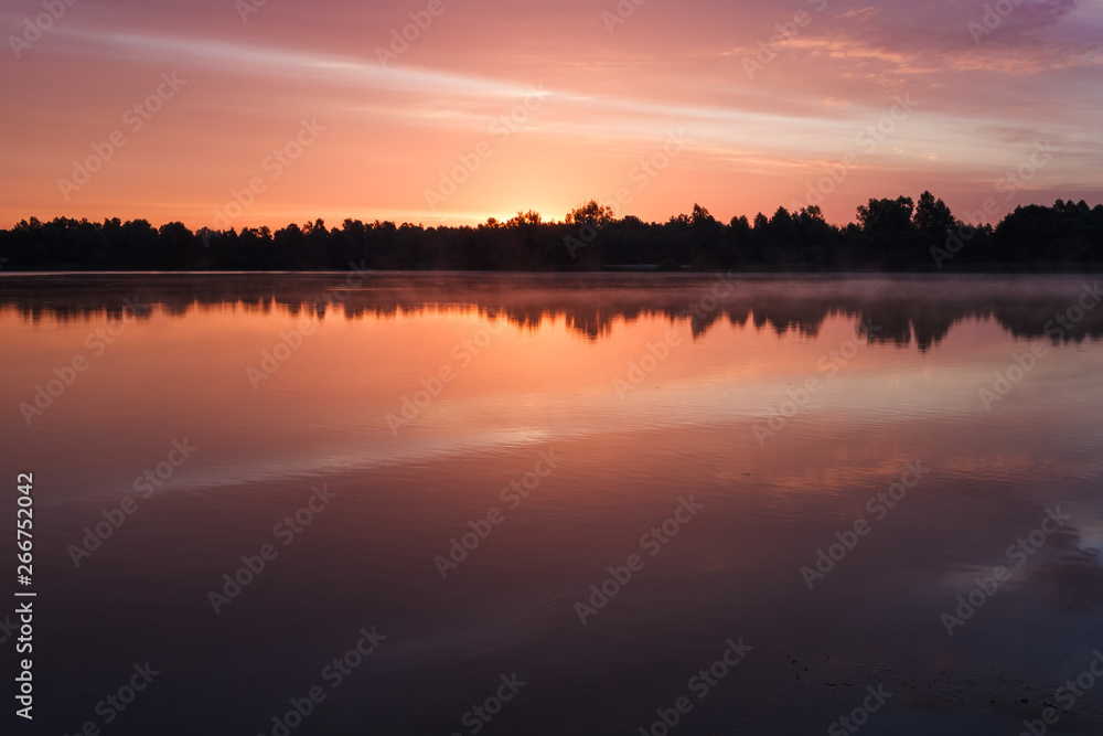 Sunrise over the forest lake. Reflection of the sky in the lake. Summer