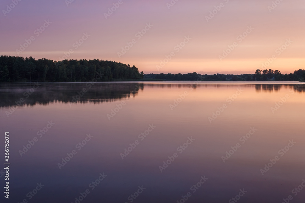 Sunrise over the forest lake. Reflection of the sky in the lake. Summer