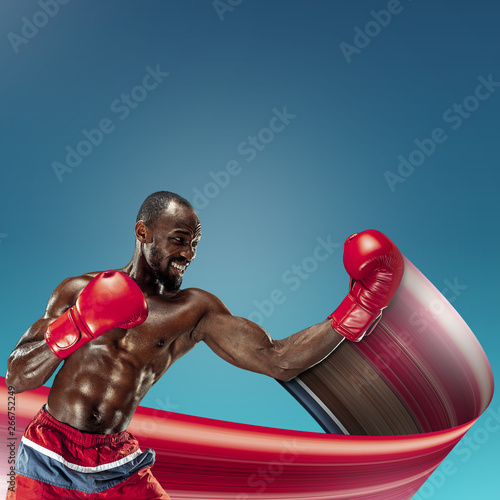 Young african-american athlete training on blue studio background. Muscular male model boxing. Concept of sport, bodybuilding, healthy lifestyle, movement, action. Abstract design.