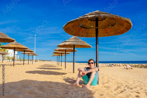 A teenage boy sitting under reed umbrella on the beach