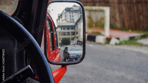 Side mirror of a red car reflecting a building © ChemaGrenda