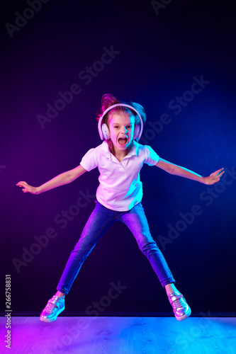 Girl of 7 years old listening to music in headphones and jump on dark colorful background . Dancing girl. Happy small girl dancing to music. Cute child enjoying happy dance music.