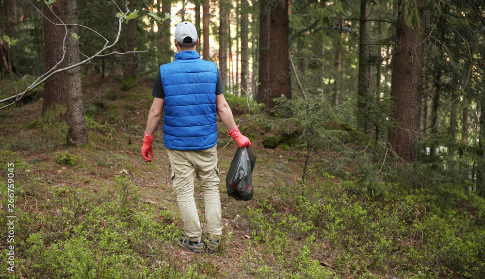 Adult man volunteer in red gloves removes plastic trash in forest, caring for environment. Adult man volunteer in red gloves removes plastic trash in forest, caring for environment.