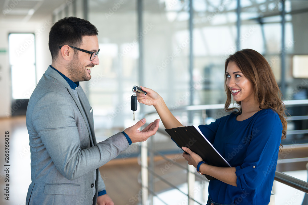 Vehicle dealer giving keys to the car buyer in showroom. Automobile dealership. Vehicle dealer giving keys to the car buyer in showroom. Automobile dealership.