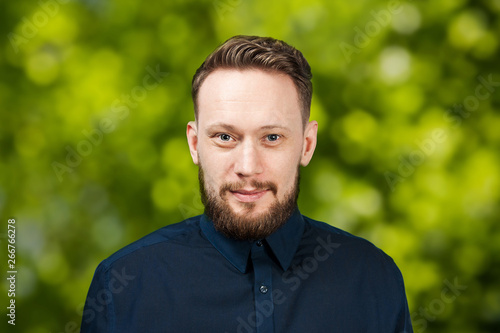 Portrait of handsome adult man on green bokeh background. Caucasian man with beard smiling. Businessman.