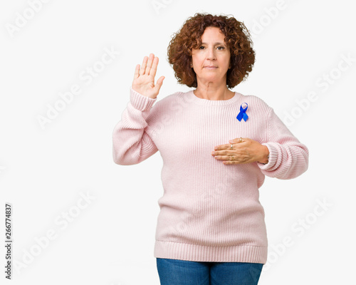 Middle ager senior woman wearing changeable blue color ribbon awareness over isolated background Swearing with hand on chest and open palm, making a loyalty promise oath
