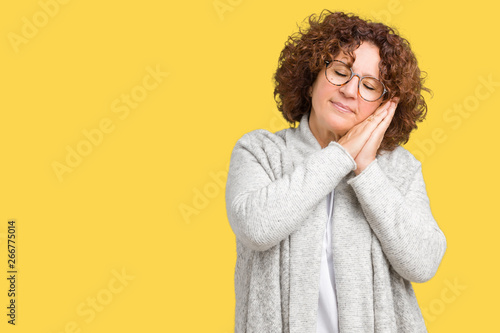 Beautiful middle ager senior woman wearing jacket and glasses over isolated background sleeping tired dreaming and posing with hands together while smiling with closed eyes.