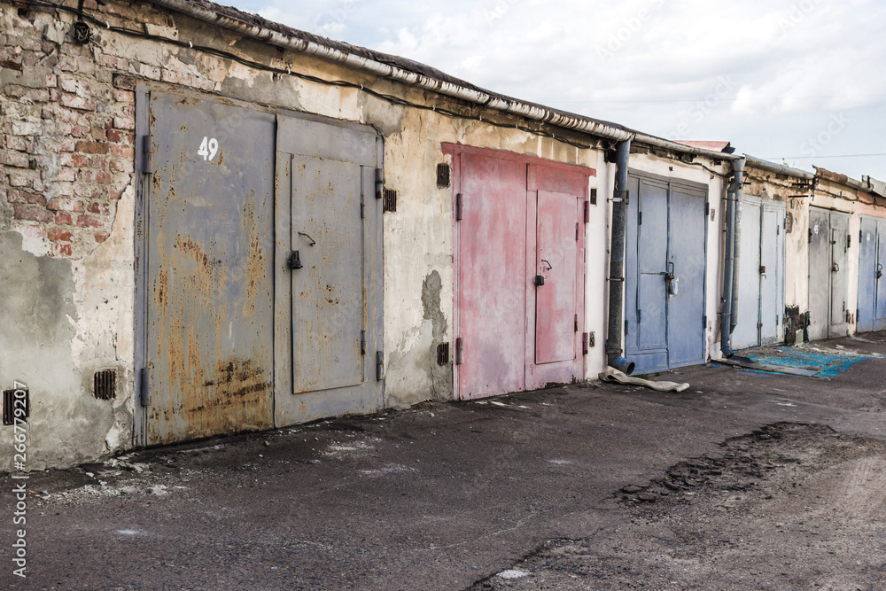 Garage cooperative. Rows of car garages. City architecture. Transport industry. Stone sheds. Rusty iron gate. Brick wall. Perspective in architecture. Abandoned area. Deserted street.